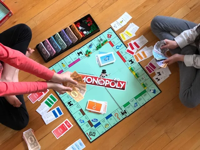 Die 10 besten Monopoly-Editionen – außergewöhnliche Varianten des beliebten Brettspiels 2 Monopoly Brettspiel auf dem Boden mit Spielern, Geldscheinen und Karten während eines Spieleabends