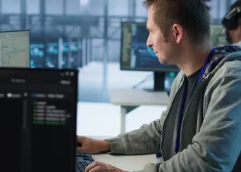 Fachinformatiker für Systemintegration arbeitet an mehreren Monitoren in einem Serverraum und überwacht Netzwerksysteme