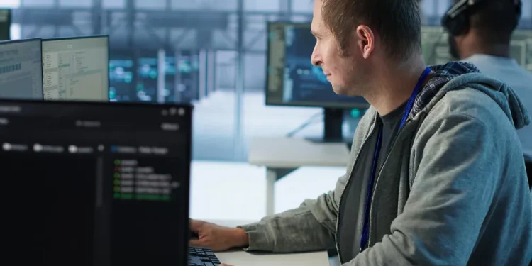 Fachinformatiker für Systemintegration arbeitet an mehreren Monitoren in einem Serverraum und überwacht Netzwerksysteme