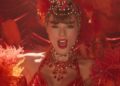 Taylor Swift in funkelndem roten Showgirl-Kostüm mit Federkopfschmuck und Kristallschmuck, Nahaufnahme auf einer Bühne mit warmem Rotlicht.