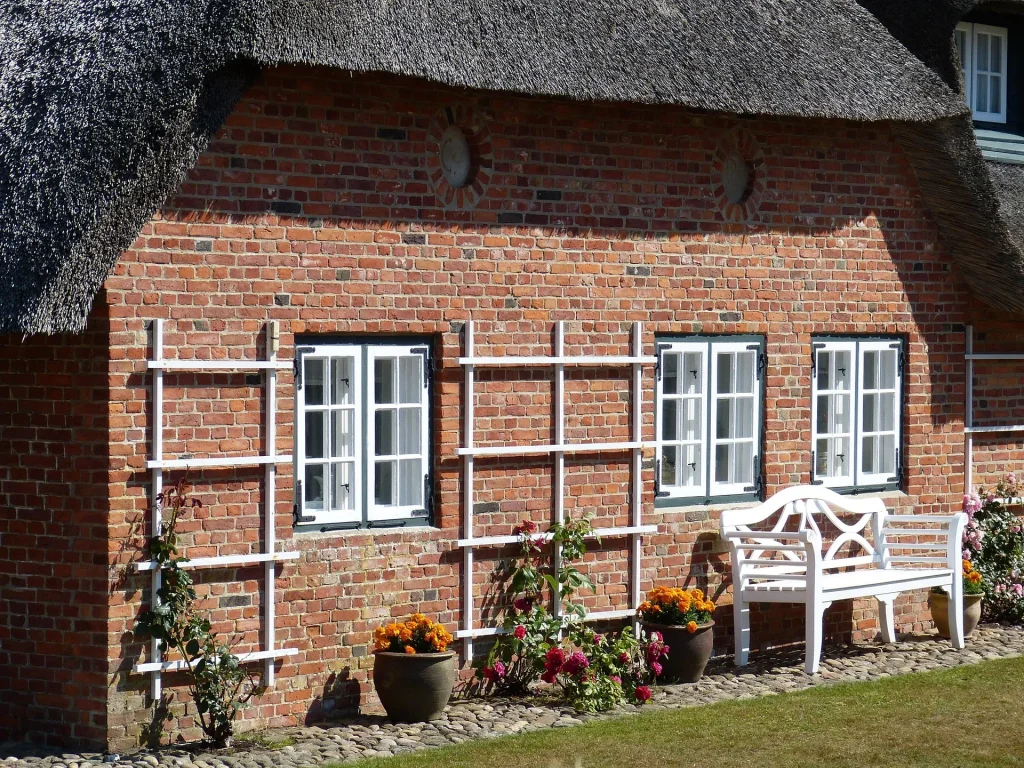 Immobilien-Flut auf Sylt: Warum plötzlich Hunderte Häuser zum Verkauf stehen 3 Reetdachhaus auf Sylt mit Klinkerfassade und weißer Sitzbank vor dem Gebäude
