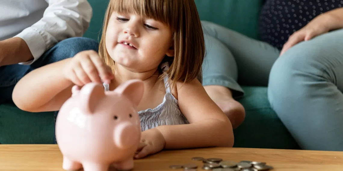 Frühstartrente: Der Staat zahlt 10 Euro für Kinder – daraus könnten 53.000 Euro werden 1 Kind wirft Münzen in ein Sparschwein – Symbolbild für die Frühstartrente und staatlich geförderte Altersvorsorge für Kinder.